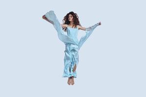 Flying high.... Full length studio shot of attractive young woman in elegant dress gesturing while hovering against grey background photo