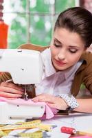 todo debe ser perfecto. diseñadora de moda femenina segura de sí misma trabajando en una máquina de coser mientras se sienta en su lugar de trabajo foto