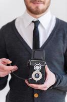 Man with old style camera. Cropped image of young man holding a retro camera while standing against grey background photo