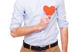 I am in love Close-up of young man holding heart shaped valentine card in front of his heart while standing isolated on white background photo