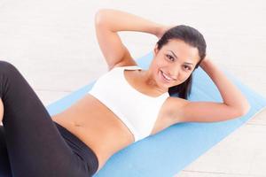 Woman working out. Top view of cheerful young Indian woman training on yoga mat photo