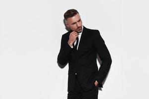 Thinking about solution. Handsome young man in full suit keeping hand in pocket and looking away while standing against white background photo