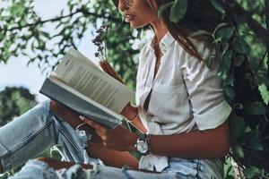 Close-up of young woman holding an open book while sitting on the tree outdoors photo