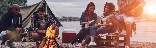 Playing favorite song. Group of young people in casual wear smiling while enjoying beach party near the campfire photo