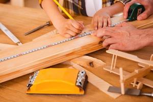 Working process. Seriousboy making measurements on the wooden plank while his father helping him photo