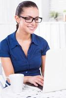 Surfing the net in cafe. Beautiful young woman working on laptop and smiling while sitting in cafe photo