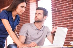Business consulting. Handsome young man sitting at his working place and pointing computer while confident woman standing close to him photo