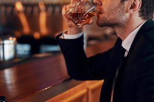 Close-up of young man in suit drinking whiskey while sitting at the bar counter in restaurant photo