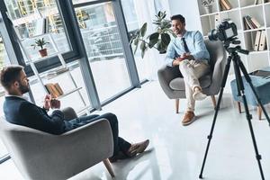 Business vlog. Two young men in smart casual wear talking while making new video indoors photo