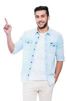 Look at that Confident young Indian man pointing copy space and smiling while standing against white background photo