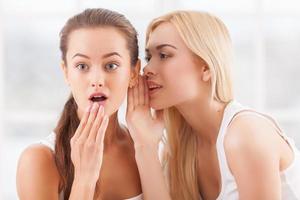 Telling the hottest gossips. Two beautiful young women gossiping while one of them covering mouth with hand photo