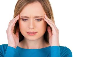 Awful headache. Frustrated young woman touching head with hands and looking down while standing isolated on white photo