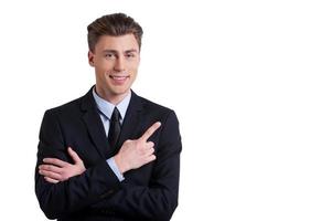 Pointing copy space. Cheerful young man in formalwear keeping arms crossed and pointing away while standing isolated on white photo