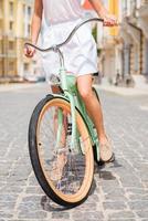 Exploring town by bike. Close-up of young woman riding bicycle along the street photo