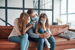 Young family with preschool age girl wearing protective face masks while bonding together at home photo