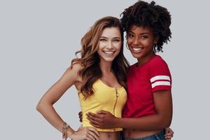 Two attractive young women looking at camera and smiling while standing against grey background photo