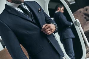 Confident in his style. Close up of young man in full suit adjusting jacket while standing indoors photo
