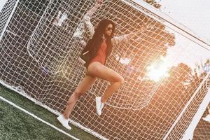 mejor portero de todos los tiempos. longitud completa de una joven atractiva en bikini rojo apoyada en la red mientras está de pie en el poste de la portería al aire libre foto