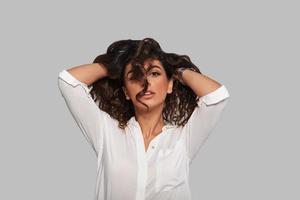 Made to be a model. Attractive young woman playing with her hair and looking at camera while standing against grey background photo