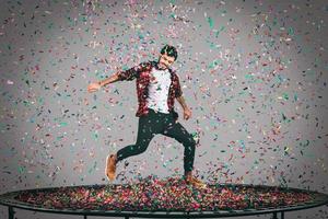 Trampoline and confetti. Mid-air shot of handsome young man jumping on trampoline with confetti all around him photo