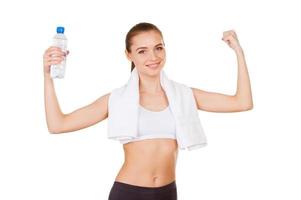 Water is life. Beautiful young woman in sports clothing holding a bottle with water and gesturing while standing isolated on white photo