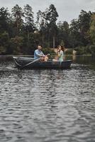 Exploring the new place. Beautiful young couple enjoying romantic date and smiling while rowing a boat photo