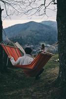 Perfect place to stay. Rear view of young man sitting in hammock while camping with his girlfriend photo