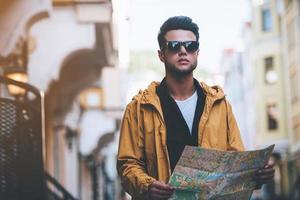 Discovering new places. Handsome young man holding map and looking away while standing on the city street photo