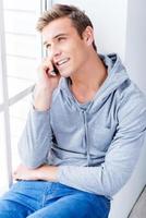 Making some urgent notes. Confident young man writing something in his note pad while sitting on the window sill photo