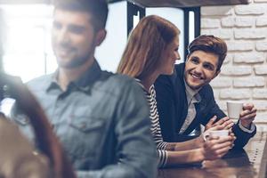 Time for coffee. Side view of young handsome man holding coffee cup and discussing something with young woman while standing at bar counter photo