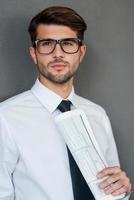 Thinking about new solutions. Confident young man in shirt and tie holding newspaper and looking away while standing against grey background photo