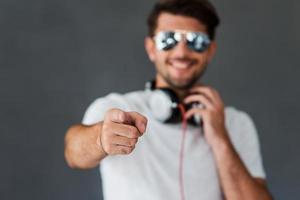 Do you like my style Happy young man in headphones pointing you and smiling while standing against grey background photo