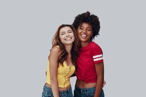 Two attractive young women looking at camera and smiling while standing against grey background photo