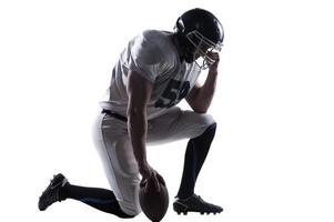 Preparing to big game. Side view of American football player holding hand on helmet while standing on knee against white background photo