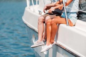 Spending great summer day together. Close-up of young couple sitting on the board of yacht photo