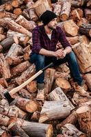 Taking smoking pause. Full length of pensive young forester smoking and looking away while sitting on logs photo