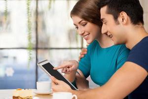 Couple with digital tablet. Side view of cheerful young loving couple sitting at the restaurant and using digital tablet photo