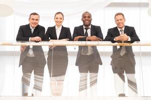 equipo de negocios vista de ángulo bajo de cuatro empresarios confiados parados uno cerca del otro y sonriendo a la cámara foto