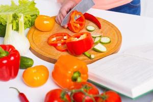 Cooking by recipe from cookbook. Close-up of woman cutting vegetable on the cutting board photo