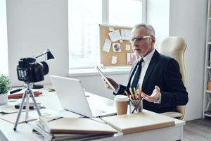 Senior man in elegant business suit using modern technologies while making social media video photo