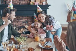 Happy family celebrating birthday of little girl while sitting at the dining table at home photo