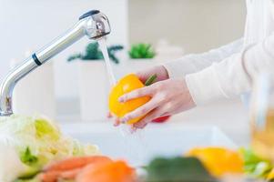 Woman washing vegetables. Beautiful young woman washing vegetables for salad and smiling while standing in the kitchen photo