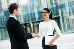 Welcome on board  Two smiling young business people shaking hands while standing outdoors photo