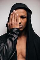 Confident in his style. Confident young African man in hooded shirt looking at camera while standing against grey background photo