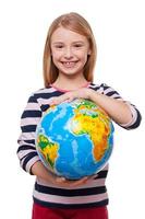 World in my hands Cheerful little girl holding a globe and smiling while standing isolated on white photo