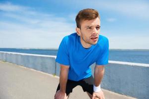 Tired of running. Tired young man holding hands on knees and looking away while standing outdoors photo