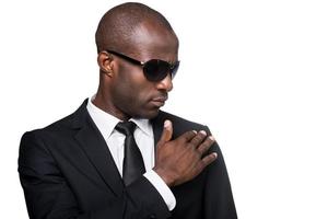 buscando simplemente perfecto. retrato de un joven africano serio con ropa formal y gafas de sol ajustando su chaqueta mientras está aislado de fondo blanco foto