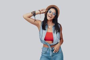 Attractive stylish young woman looking at camera and smiling while standing against grey background photo