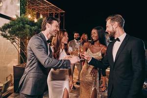 grupo de personas en ropa formal comunicándose y sonriendo mientras pasan tiempo en una fiesta de lujo foto