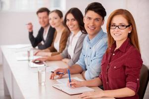 personas trabajando juntas. grupo de jóvenes sentados juntos en la mesa y sonriendo a la cámara foto